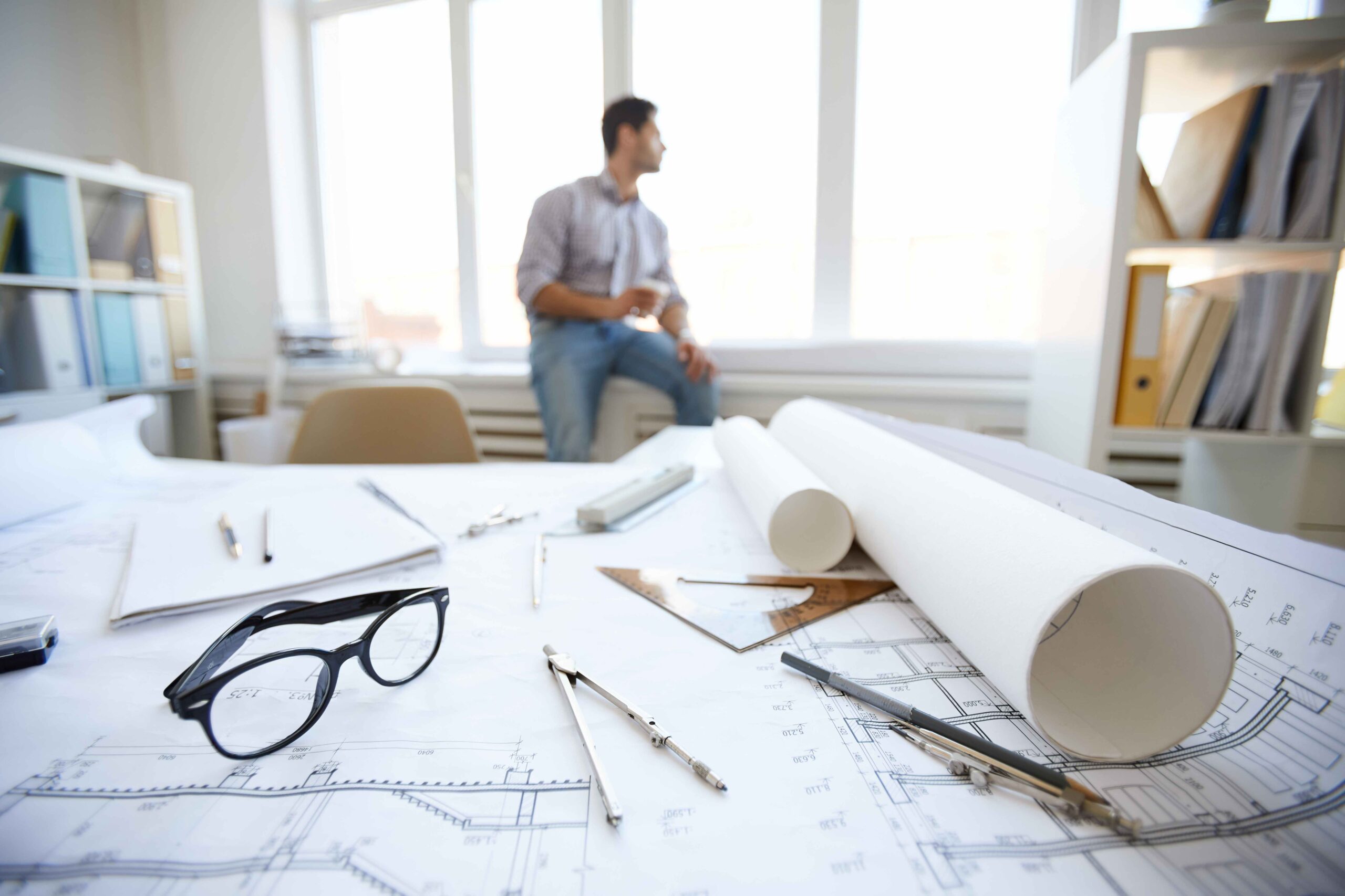 Background of engineers tools and plans on desk with man resting in background, copy space